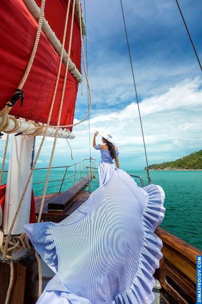 Woman in blue dress on sailboat, Lisbon coast. Ocean view, red sails, summer travel.
