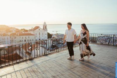 Couple holding hands overlooking Lisbon, Portugal. Alfama rooftops and Tagus River in the background. Golden hour light.