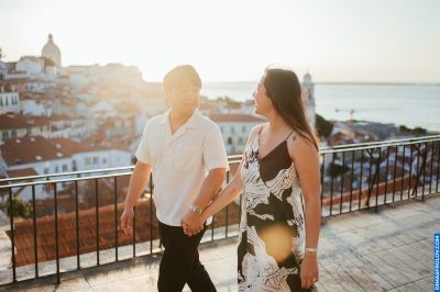Couple holding hands in Lisbon, Portugal. Alfama district with red rooftops and Tagus River in background. Golden hour.