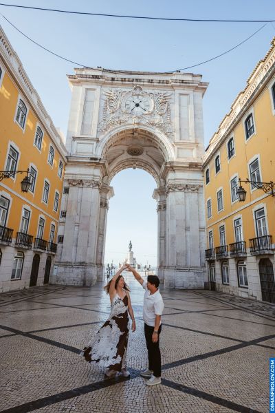 Couple dancing under the Rua Augusta Arch in Lisbon, Portugal. Yellow buildings and patterned cobblestone streets. Romantic Lisbon scene.