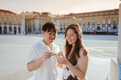 Couple sharing a Pastel de Nata in Lisbon-s Praça do Comércio. Enjoying Portuguese pastry. Travel in Portugal.