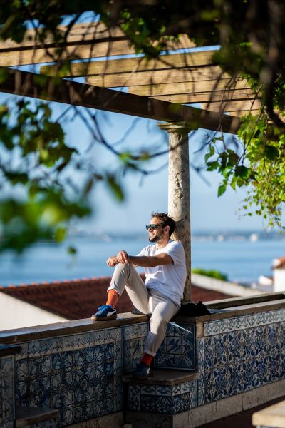 Man relaxes on tiled wall overlooking the Tagus River in Lisbon, Portugal. Sunny day, Alfama vibes.