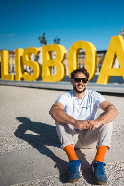 Man sits by -Lisboa- sign in Lisbon, Portugal. Sunny day, blue sky. Tourism in Portugal.