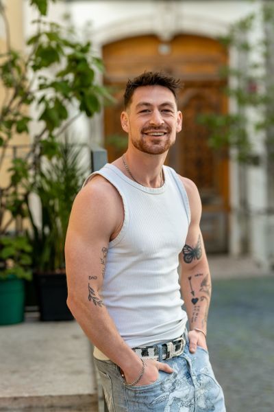 Tattoed man in Lisbon. Smiling man in tank top and printed jeans, Lisbon street background. Portugal travel.