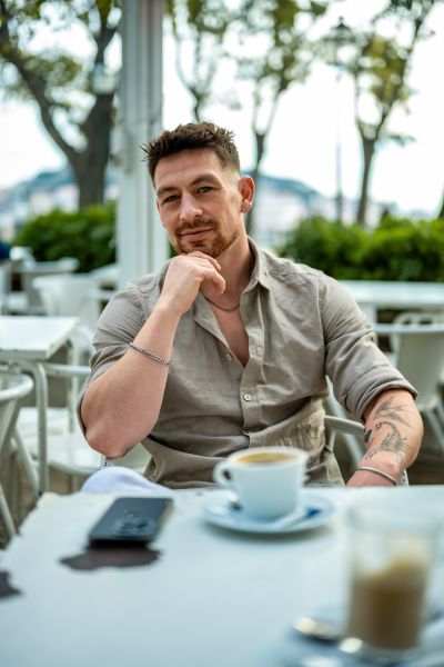 Man with coffee in Lisbon. Outdoor cafe scene. Tattoos, relaxed pose. Lisbon vibes.