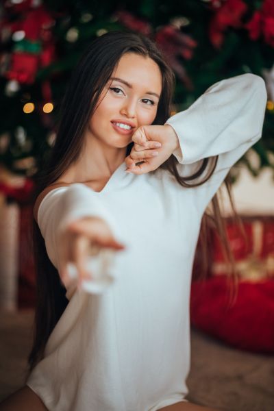 Woman in white sweater smiling in front of a Christmas tree.