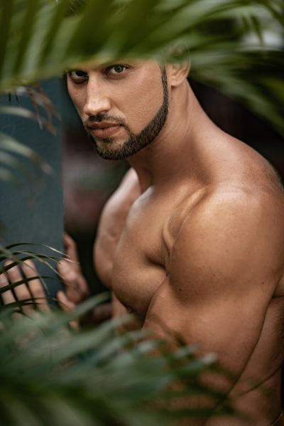 Muscular man portrait in Lisbon, framed by lush foliage. Exotic, sensual, and mysterious.
