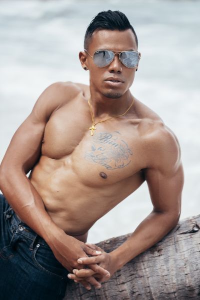 Muscular man with sunglasses in Lisbon. Ocean reflection in glasses. Tattoos, gold chain. Beach vibes. Men-s fashion.