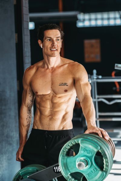 Fit man in Lisbon gym. Muscular build, tattoos, and earbuds. Weightlifting in a modern Portuguese fitness center.