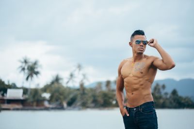 Shirtless man with sunglasses poses in Lisbon. Ocean view, casual style. Portugal travel.