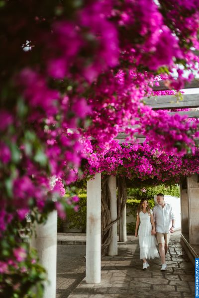 Couple walks under bougainvillea in Lisbon, Portugal. Romantic stroll in a garden setting.