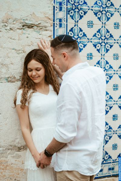 Couple in Lisbon. Woman in white dress, man in kippah. Blue & white tiles, stone wall. Romantic moment in Portugal.