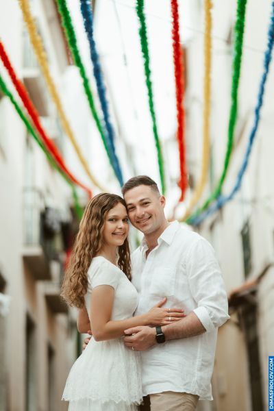 Couple embraces in Lisbon street, colorful streamers above. Romantic moment in Portugal.