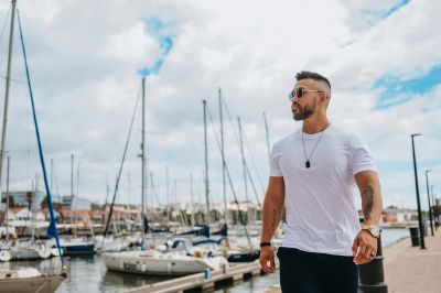 Stylish man in Lisbon marina. Sailboats & waterfront buildings in background. Portugal travel.
